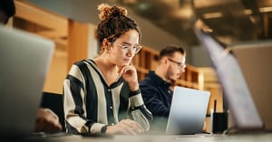 Female wearing glasses looking at her laptop screen with her hand on her chin